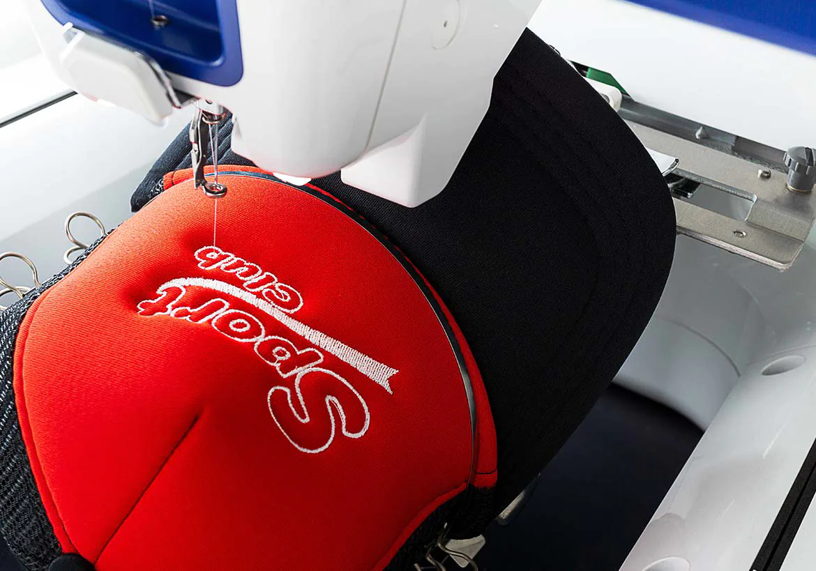 Close-up of embroidery machine stitching custom red lettering on fabric, showcasing precision in custom embroidery and apparel decoration – Custom Apparel, Screenprinting, and Embroidery services in Los Angeles.